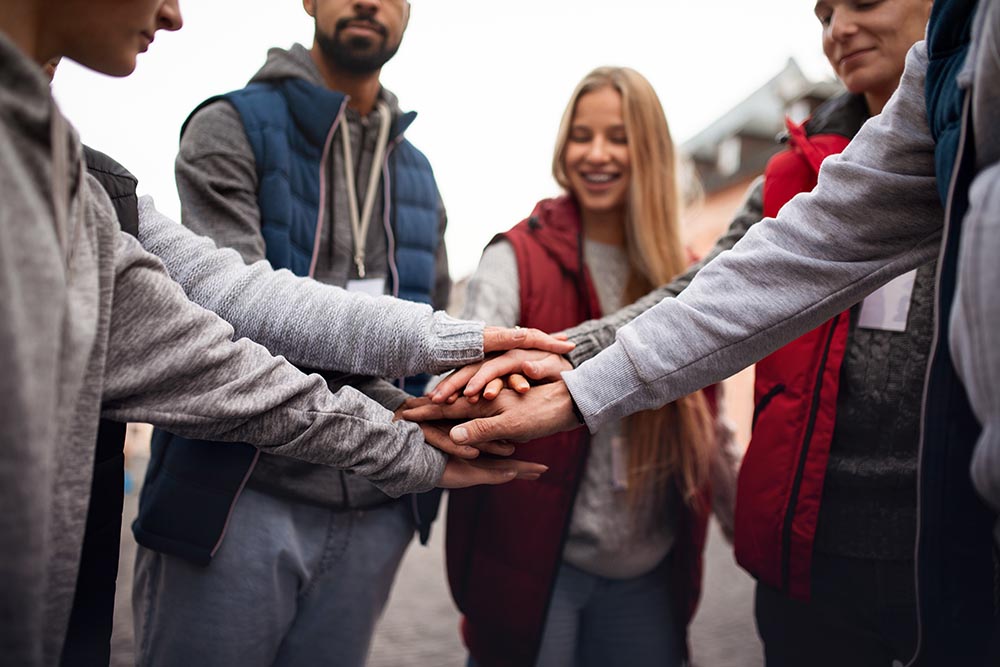 Close up of group of happy community service volunteers stacking hands together outdoors in street Smiling Store Clerk with Customers
